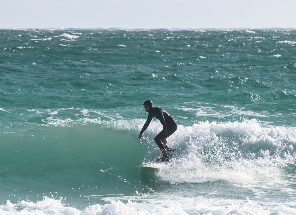 Surfer in a hooded wetsuit riding a cold-water wave.